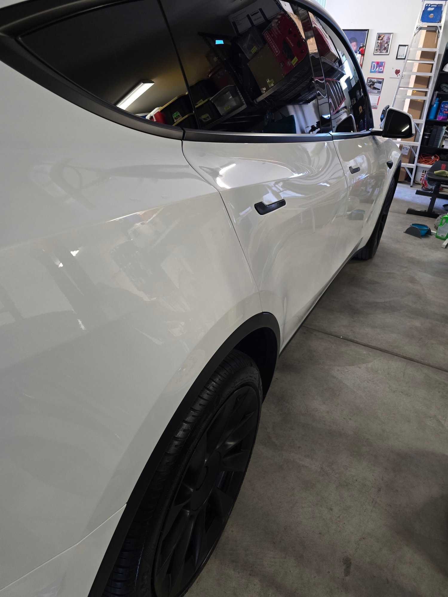Glossy white Tesla side panel reflecting a hangar interior after paint correction.