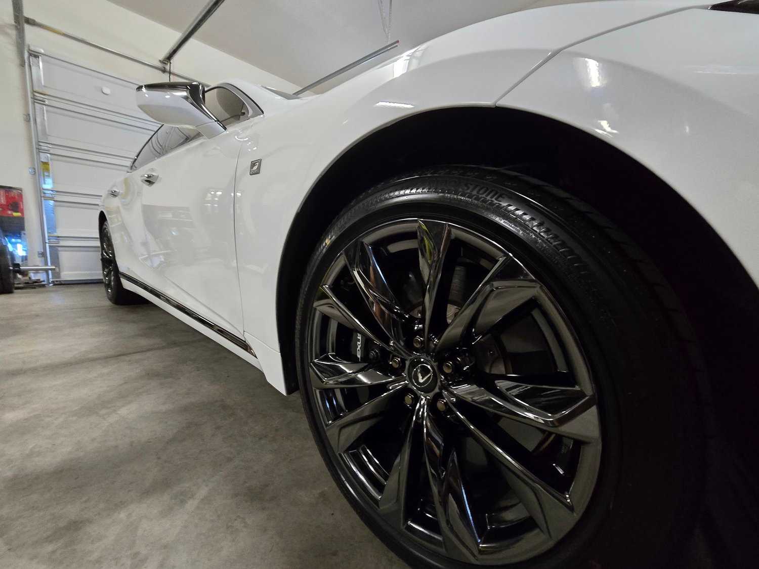 Close-up of a polished black wheel and white Lexus side panel showing reflection of the hangar after a detail.