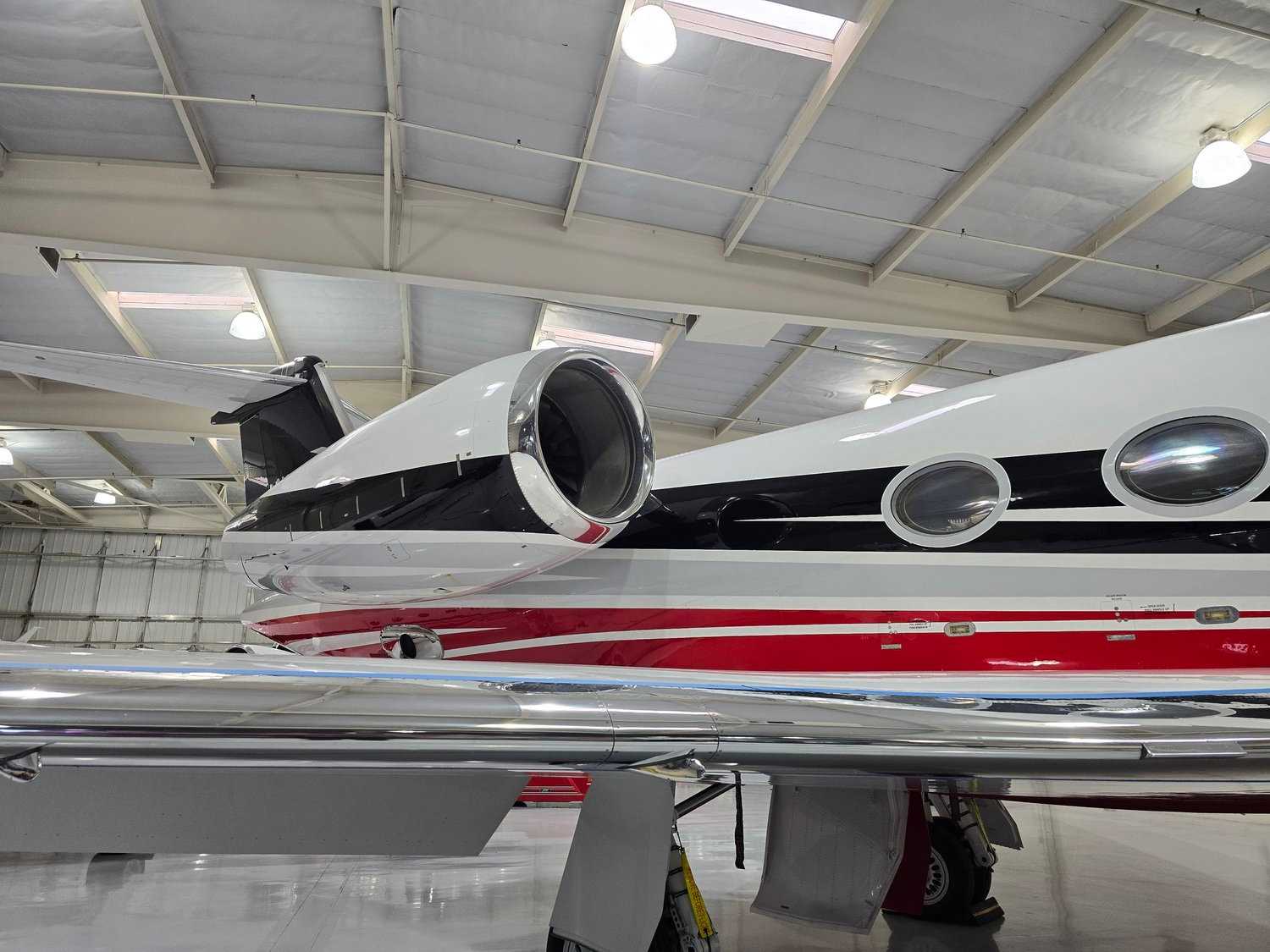 Engine and rear fuselage of a red and white private jet inside a hangar after exterior detailing.