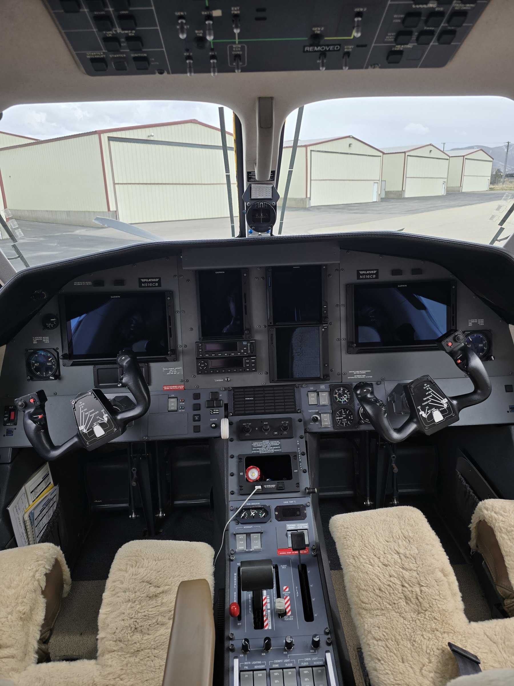 Clean aircraft cockpit with sheepskin seat covers and a glass instrument panel.