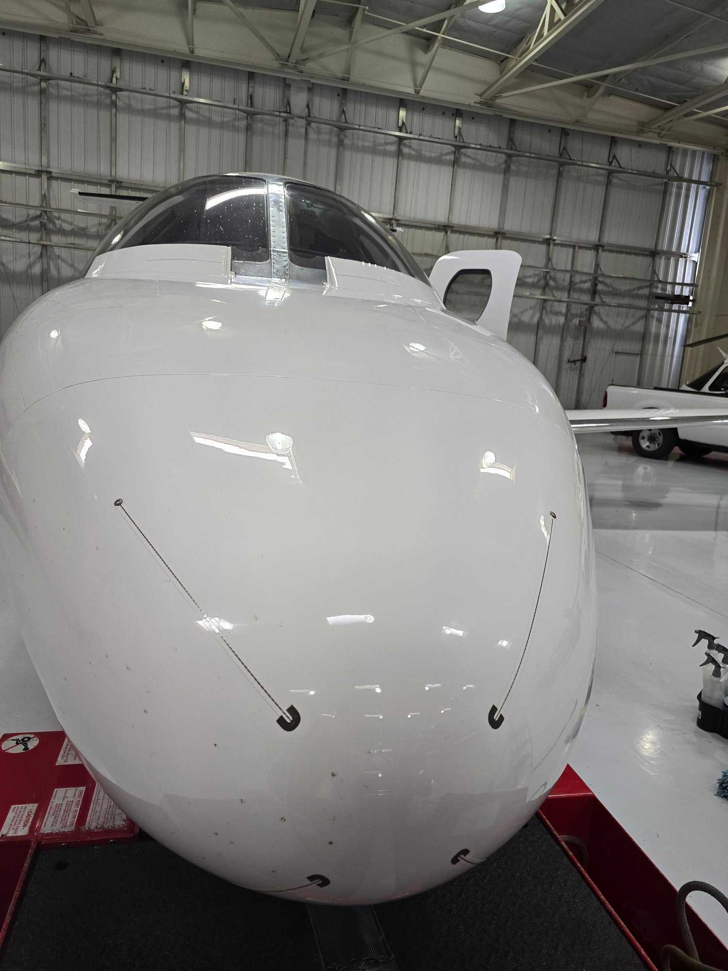 Close-up of a clean white aircraft nose with cockpit window inside a Las Vegas hangar.