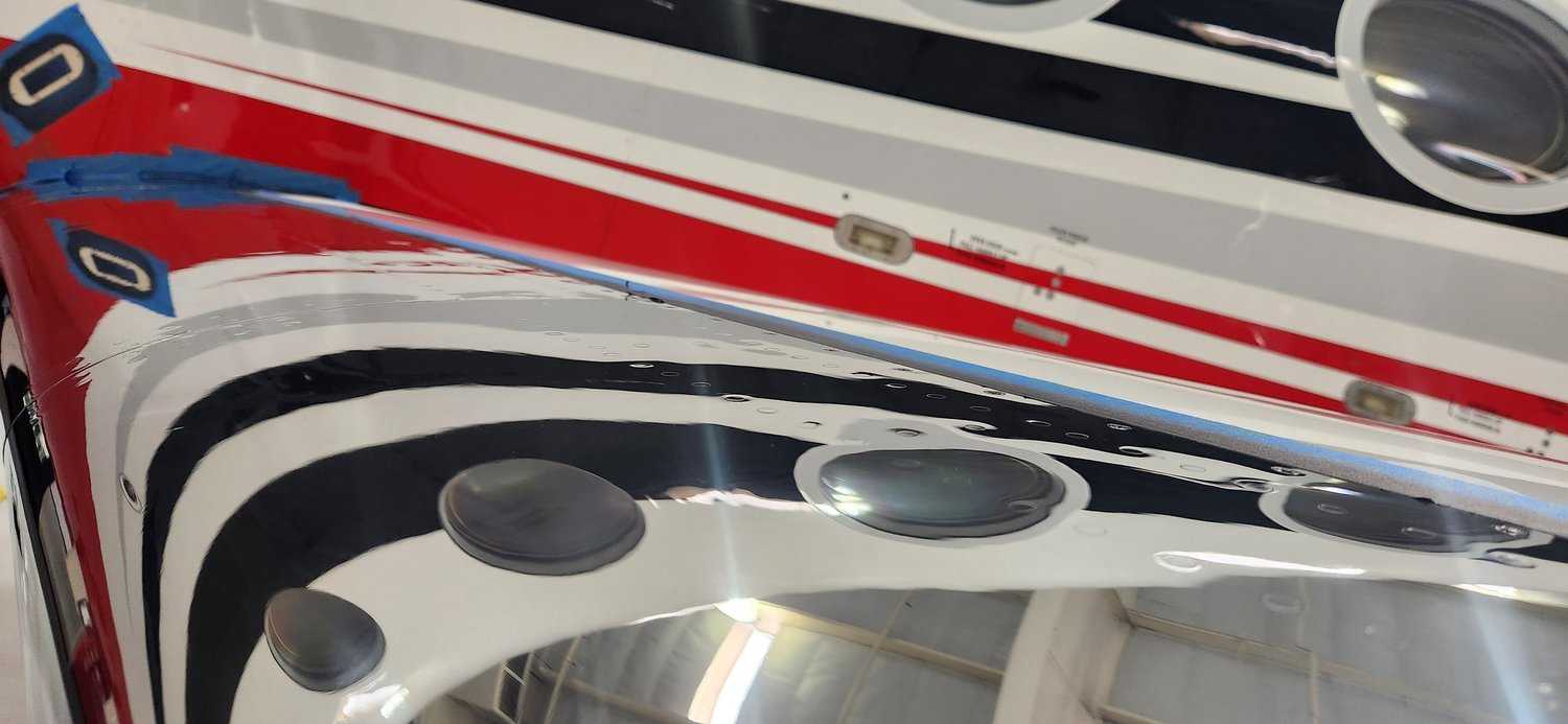 Close-up of red, black, and white aircraft fuselage with mirror-finish reflection from windows.