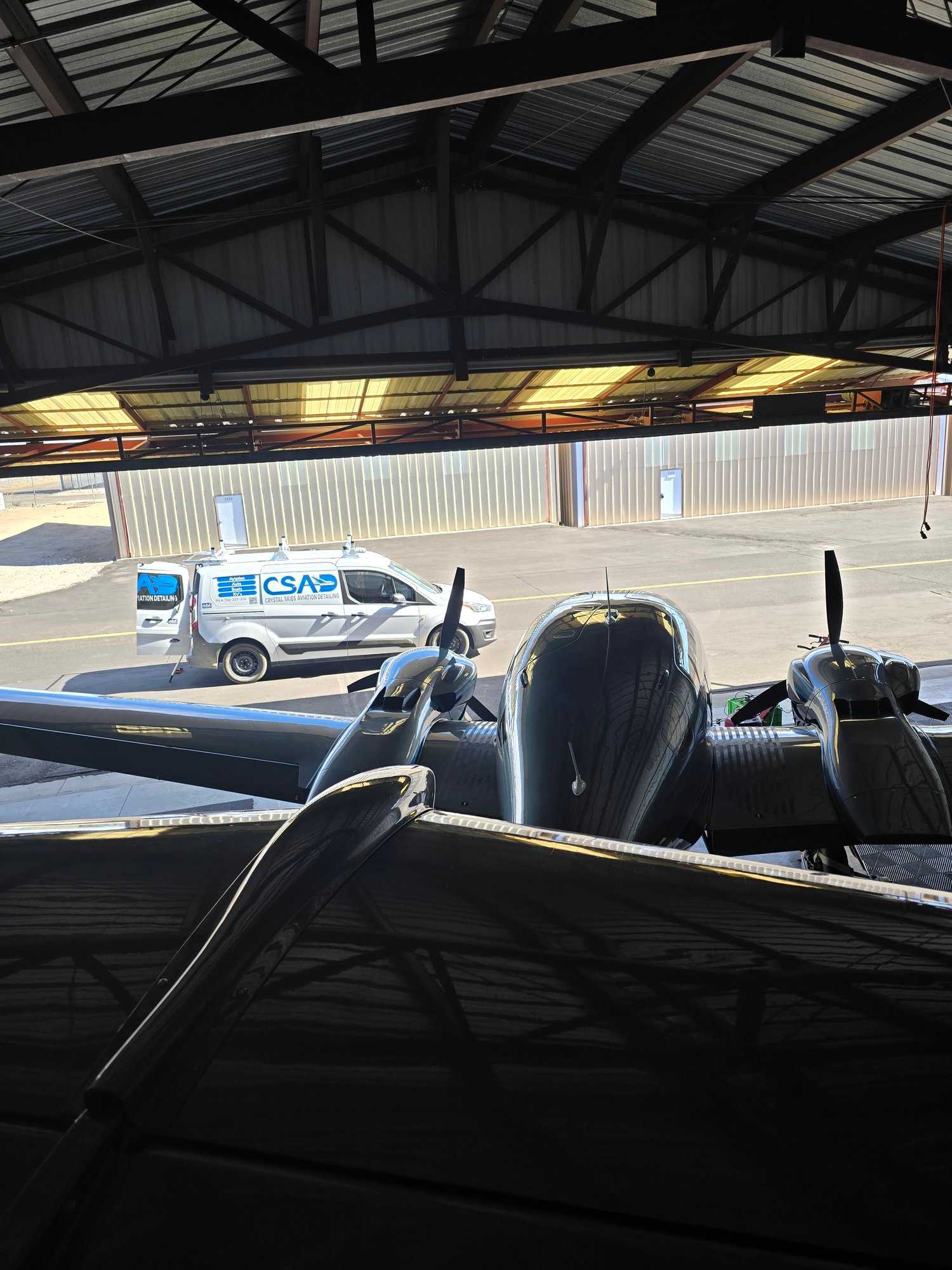 Crystal Skies service van parked beside a vintage twin-engine aircraft inside a hangar.