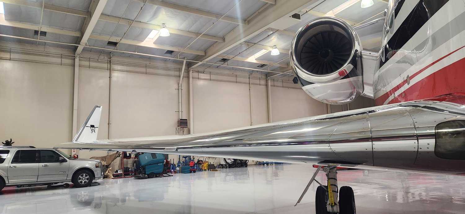 Reflective polished wing and engine of a red and white private jet inside a Las Vegas hangar.